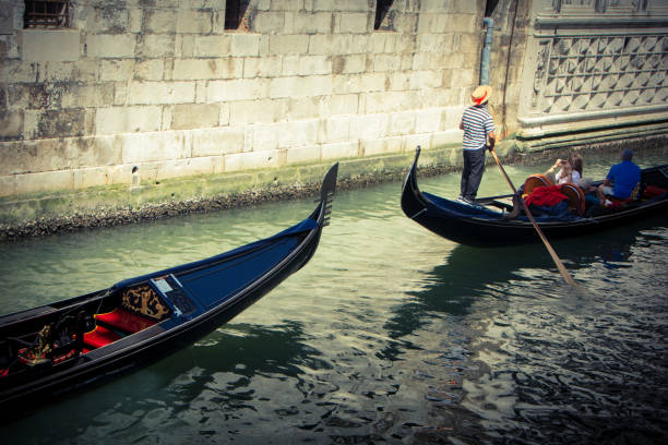 Gondola in Venice Venice, Italy - July 9, 2018 : Black gondolas moving through the water canal with the tourists inside. Venice is a one of the most famous travel destination in the world, a city in northeastern Italy and the capital of the Veneto region. Gondola is a traditional, flat-bottomed Venetian rowing boat, well suited to the conditions of the Venetian lagoon.Their primary role today is to carry tourists on rides. venice italy grand canal honeymoon gondola stock pictures, royalty-free photos & images