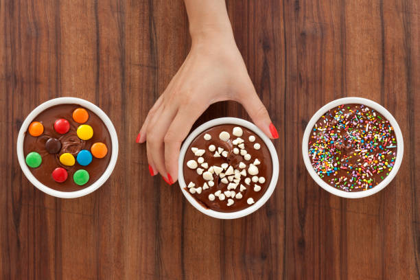 Offering chocolate desserts with toppings Top view of three bowls with varieties of chocolate desserts with toppings with female hand holding the one in the middle chocolate white chocolate chocolate chip white stock pictures, royalty-free photos & images