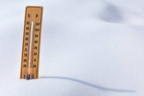 Wooden thermometer standing in the snow, sun casting curvy shadow, red column showing 0 degrees Celsius temperature. Winter / snow coming concept.