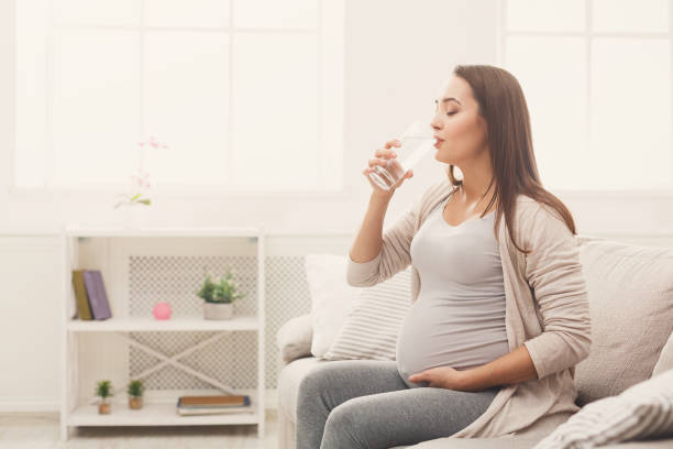 istock Pregnant woman drinking water sitting on sofa 1067084284
