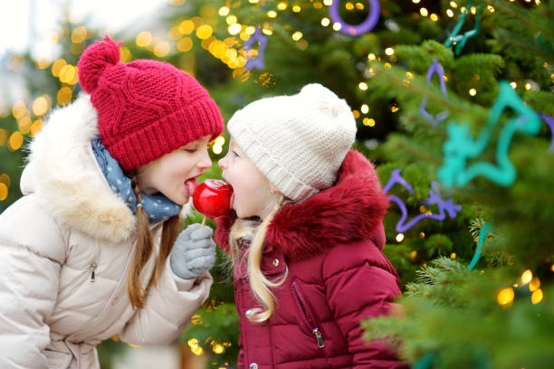 istock Two adorable little sisters eating red apples covered with sugar icing on traditional Christmas market 1067085428