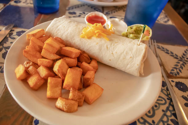 istock Yummy breakfast burrito and cubed fried potatoes on a plate on a tile table in a resturant 1067087860