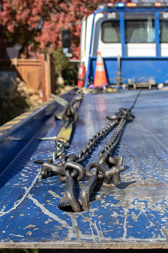 View of chains and hooks on the back of a tow truck looking from back up to the cab with orange cones and fall leaves in background - selective focus