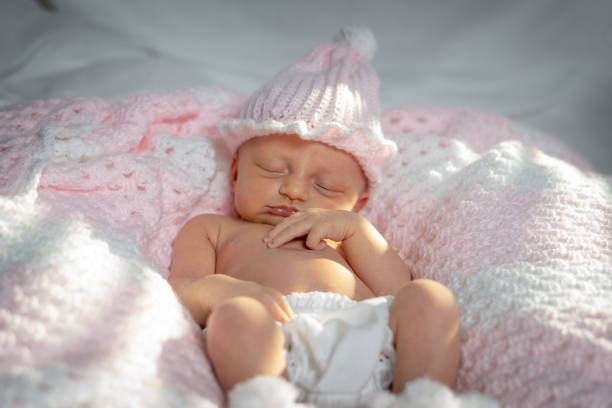 Newborn baby girl in a pink hat with two fingers over her mouth stock photo