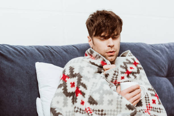 istock young sick man wrapped in blanket drinking tea in bed at home 1067101878