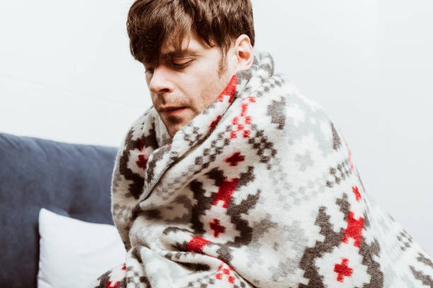 istock sick young man wrapped in blanket sitting on bed at home 1067101892