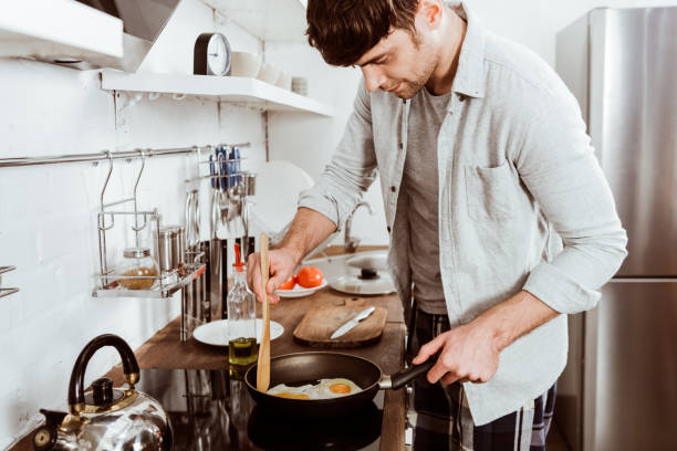 istock handsome young man making eggs on breakfast in kitchen at home 1067117366
