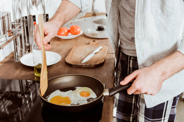 istock cropped image of young man cooking eggs on frying pan in kitchen 1067117392