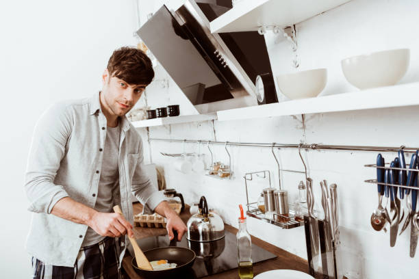 istock selective focus of young man cooking scrambled eggs on stove in kitchen 1067117402
