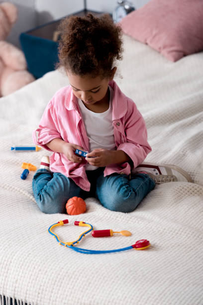 istock Curly african american kid playing with toy stethoscope on the bed 1067128580