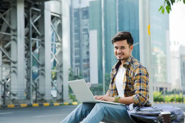 Photo of Smiling student sitting on path using laptop - Stock image