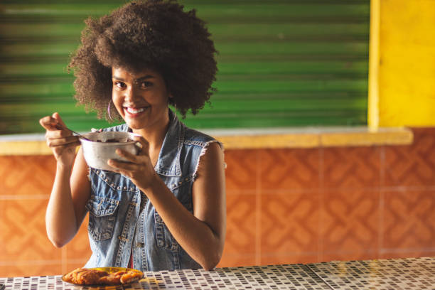 Portrait of afro brazilian woman eating fried fish with acai, a typical food combination of amazonian cuisine Portrait of afro brazilian woman, with black curly hair. Eating fried fish with acai, a typical food combination of amazonian cuisine. Smiling purple lips smeared with acai cream belém brazil stock pictures, royalty-free photos & images