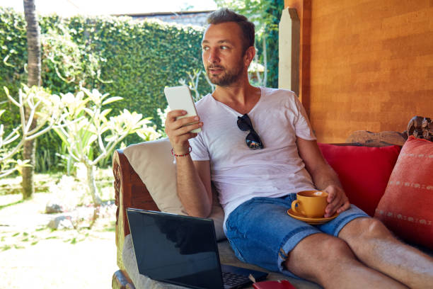 istock Man using cellphone and laptop while drinking coffee / tea on the porch. 1067163360