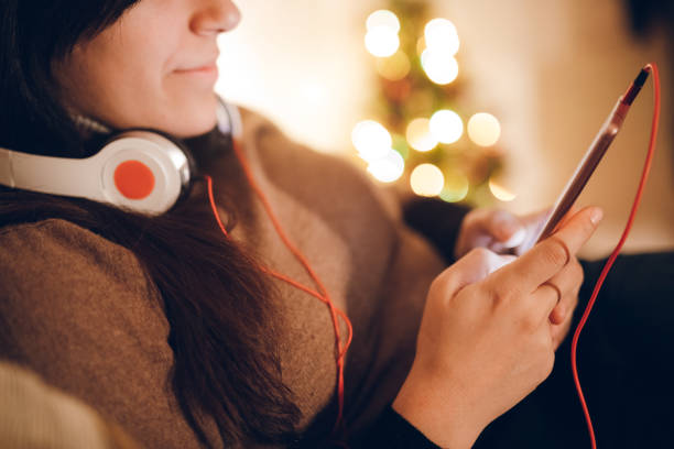 My Christmas gifts. Cheerful happy involved girl standing against the black background while expressing joy and using earphones and the mobile