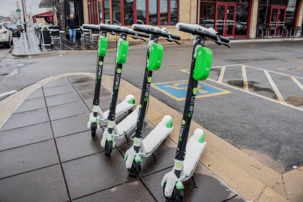 Smart personal mobility_ Four Lime electric scooters parked on the sidewalk on Cherry Street in the snow with shops and cars parked along the street and an outside cafe behind - selective focus. NOV11_12_9_2018_Tulsa OK_Smart personal mobility_ Four Lime electric scooters parked on the sidewalk on Cherry Street in the snow with shops and cars parked along the street and an outside cafe behind - selective focus. lime scooter stock pictures, royalty-free photos & images