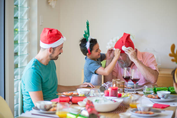 Grandson puts Christmas hat on Grandad at dining table Australian Family Christmas at home, funny hats, relationships eating child cracker asia stock pictures, royalty-free photos & images