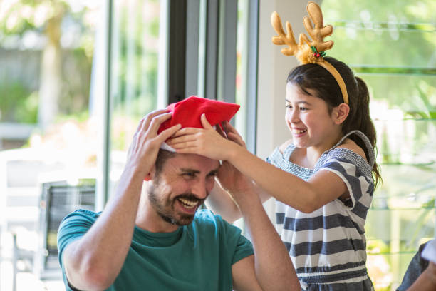 hija se pone el sombrero de la navidad en padre en mesa - eating child cracker asia fotografías e imágenes de stock