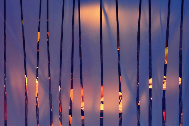 A frosted glass with vertical transparent strips, behind which there is a lighted hall, abstract interior or exterior background of yellow and purple colors