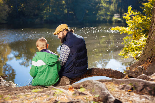 istock Nice positive man and boy sitting on the tree root 1067174592