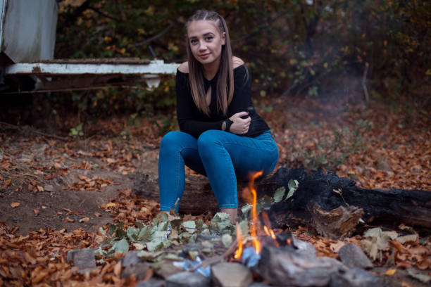 Beautiful young woman in forest sitting by the camp fire