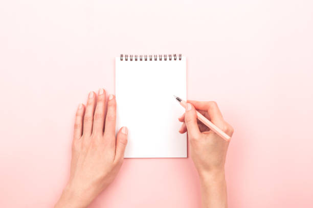 Woman hands and a notepad Woman hands are writing on notepad. Beautiful pastel pink background. Copy space for your text. female likeness photos stock pictures, royalty-free photos & images