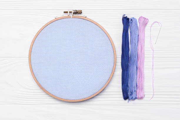istock Tools for cross stitch. Threads, a hoop for embroidery, a canvas and needle on white wooden background. 1067198474