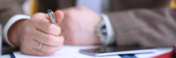 istock Male arm in suit hold phone and silver pen 1067203614