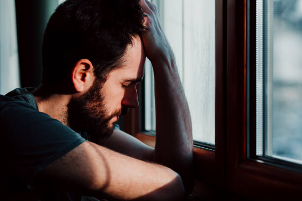 istock Bearded young man by the window in despair 1067238538