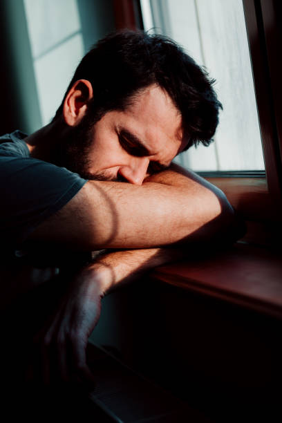 istock Bearded young man by the window in despair 1067238544