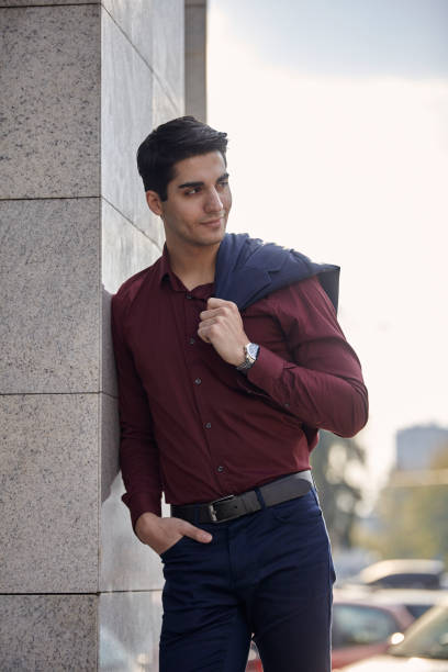 istock one young handsome man smiling, looking sideways, wearing suit, leaning on marble wall of  modern building, outdoors, sunny day. western shot. 1067252854