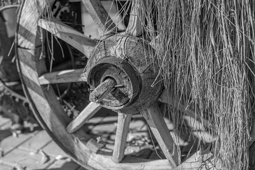 Close up of wooden wheel under dry straw and rustic background in black and white, b&w