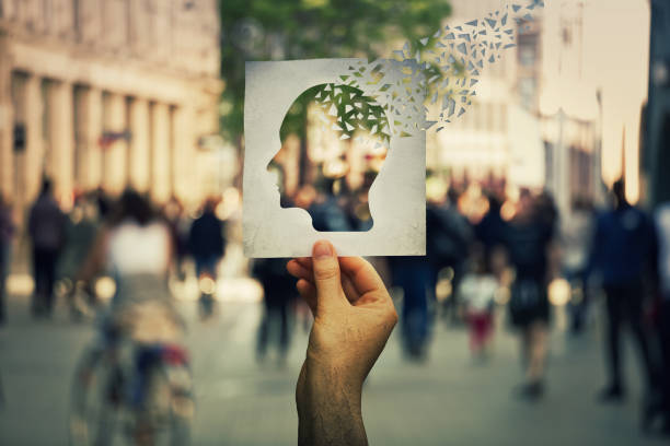 Alzheimer's losing brain Hand holding a paper sheet with human head icon broken into pieces over a crowded street background. Concept of memory loss and dementia disease. Alzheimer's losing brain and memory function. memories stock pictures, royalty-free photos & images