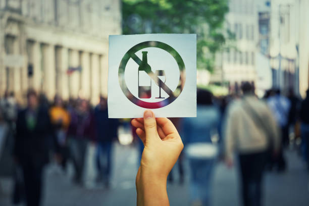 Stop to drink symbol Hand holding a paper sheet with no alcohol sign over a crowded street background. Stop to drink symbol prohibited icon. Refuse to be dependent. zoning out stock pictures, royalty-free photos & images