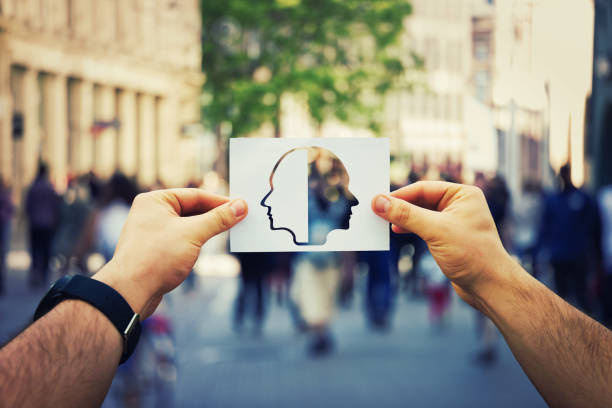 Schizophrenia psychiatric disease Man hands holding a white paper sheet with two faced head over a crowded street background. Split personality, bipolar mental health disorder concept. Schizophrenia psychiatric disease. janus head stock pictures, royalty-free photos & images