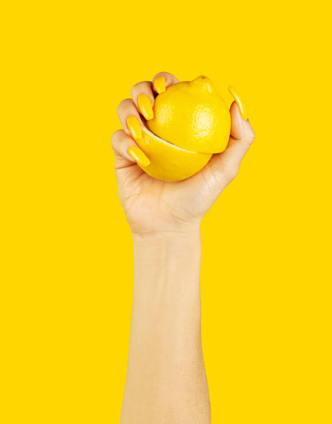 Woman with long yellow nails holding a sliced lemon Woman's hand with beautiful yellow nails, holding a closed sliced lemon against yellow background yellow nail polish stock pictures, royalty-free photos & images