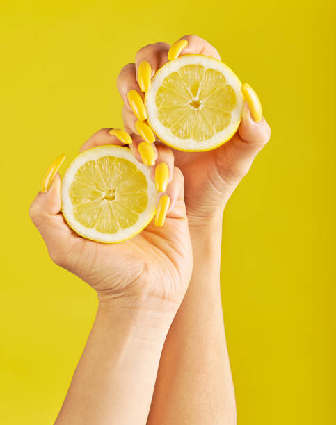 Woman with long yellow nails holding lemons Woman's hands with beautiful yellow nails, holding two slices of lemons against yellow background yellow nail polish stock pictures, royalty-free photos & images