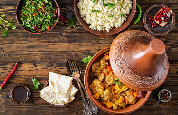 Traditional tajine dishes, couscous  and fresh salad  on rustic wooden table. Tagine lamb meat and pumpkin. Top view. Flat lay stock photo
