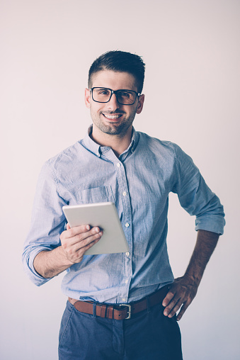 Portrait of happy businessman with digital tablet. Young Caucasian man wearing blue shirt and glasses looking at camera and smiling. Modern technology concept