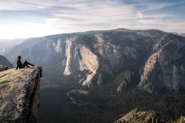 istock Fit young woman seated on a cliff edge overlooking Yosemite Valley and cliffs below 1067305750