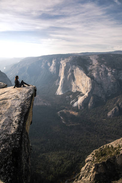 istock Fit young woman seated on a cliff edge overlooking Yosemite Valley and cliffs below 1067305800