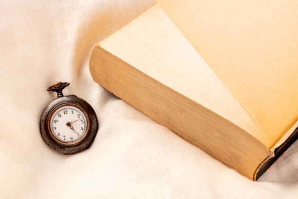 concepto de turner de página. un reloj mostrando la madrugada y un libro acabado en una almohada. imposible dejar el libro - page turner fotografías e imágenes de stock