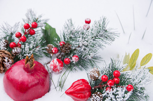 Whole pomegranate fruit and green spruce branches with cone, berries in fresh snow, winter cold time, Christmas