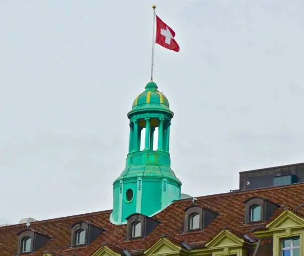 Swiss flag flies on a rooftop tower on an old building in Bern, Switzerland.