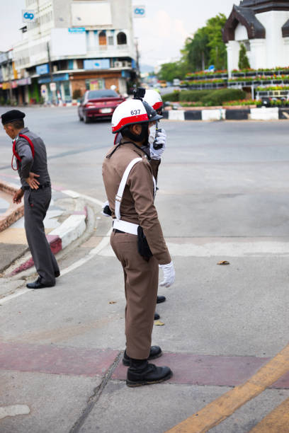 Thai traffic cops seen on street in Lampang in northern Thailand. In center cop is talking into walkietalkie. Another policeman is crossing street.