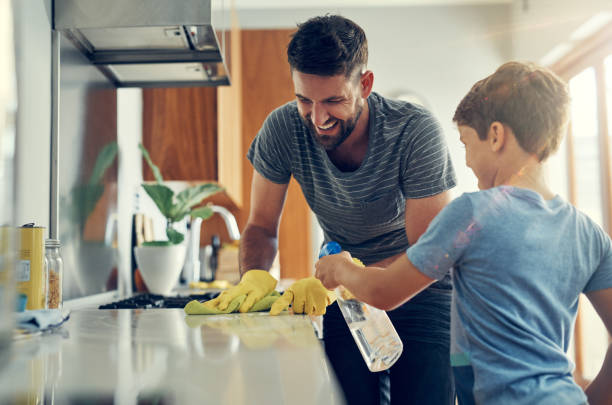 The super disinfecting son and dad duo Shot of a father and son cleaning the kitchen counter together at home kitchencleaning stock pictures, royalty-free photos & images
