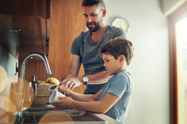 First we eat together then we clean together Shot of a father and son washing dishes together at home washing dishes photos stock pictures, royalty-free photos & images