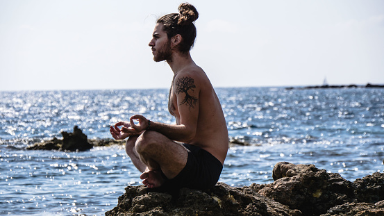 Man doing yoga poses with sea background in Ibiza Island. Praying and stretching. His mind is in a neutral position so all the calmness is by his side.