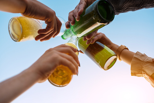 Low angle view of hands of young people toasting drinks at party. Young people partying with drinks outdoors.