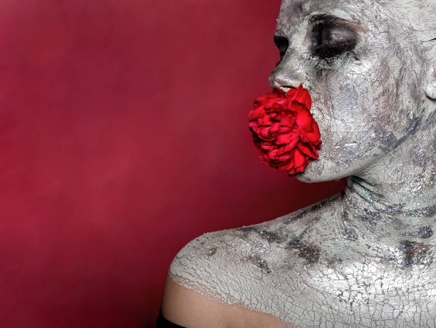 портрет девушки в серебряном макияже, глиняная маска입니다. во рту держит бутон цветка гвоздики - statue human face women human skin 뉴스 사진 이미지