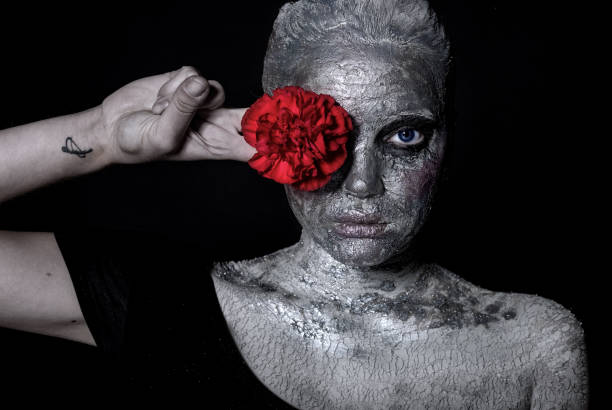 портрет девушки в серебряном макияже, глиняная маска.в руках держит бутон цветка гвоздики - women halloween statue gray fotografías e imágenes de stock